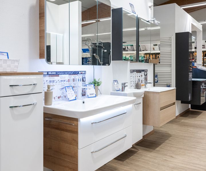 Badmöbel-Ausstellung bei bauXpert Dittmer mit modernen Waschtischunterschränken, Spiegelschränken und Armaturen auf Parkettboden