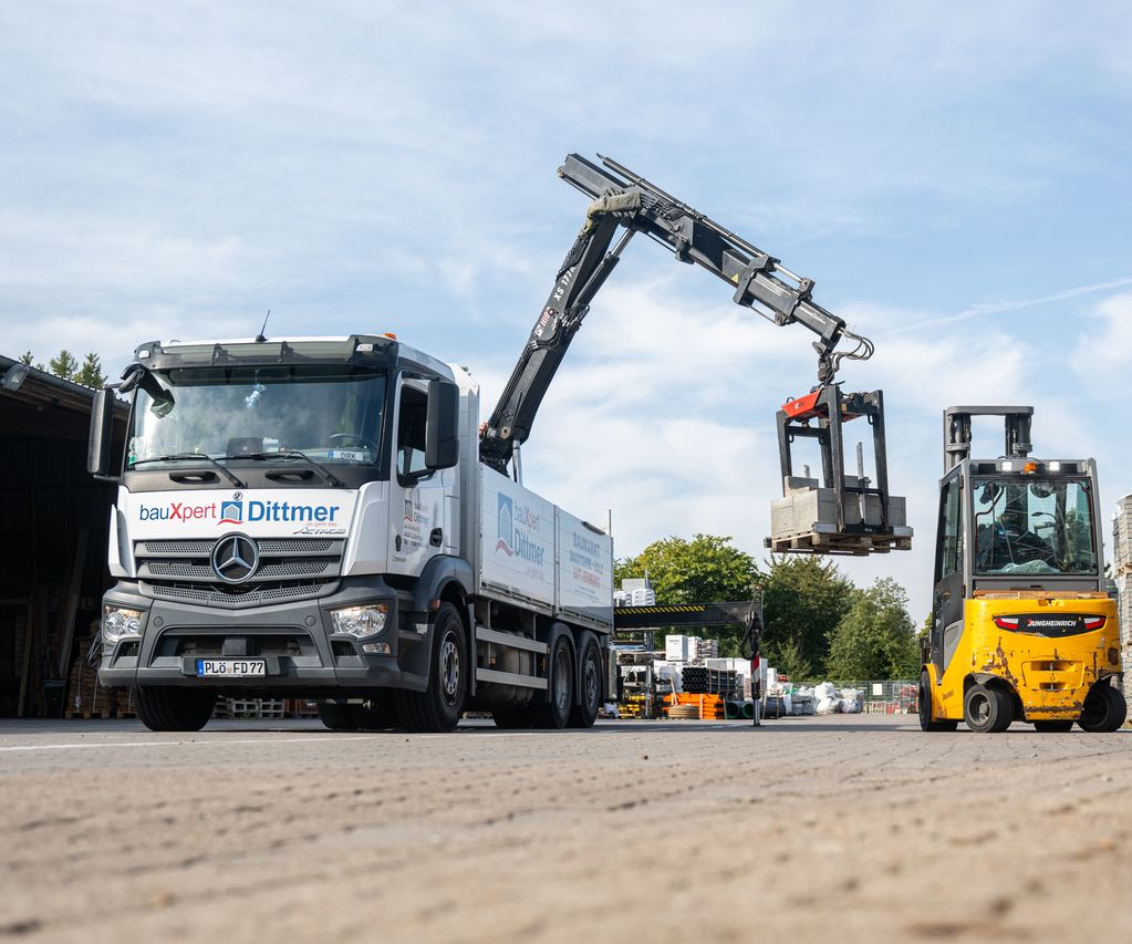 Lkw von bauXpert Dittmer mit Ladekran hebt Betonsteine von einem Gabelstapler auf dem Lagerplatz
