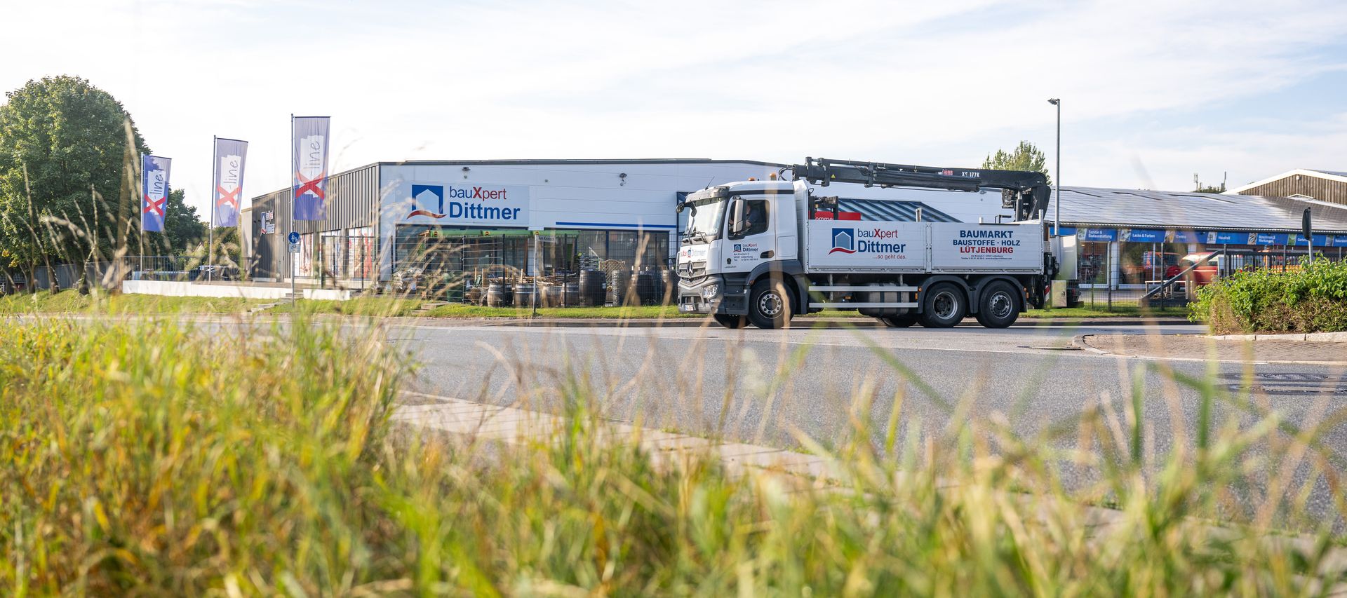 Standortansicht von bauXpert Dittmer in Lütjenburg mit Firmen-LKW im Vordergrund, Firmengebäude und Xline-Fahnen im Hintergrund