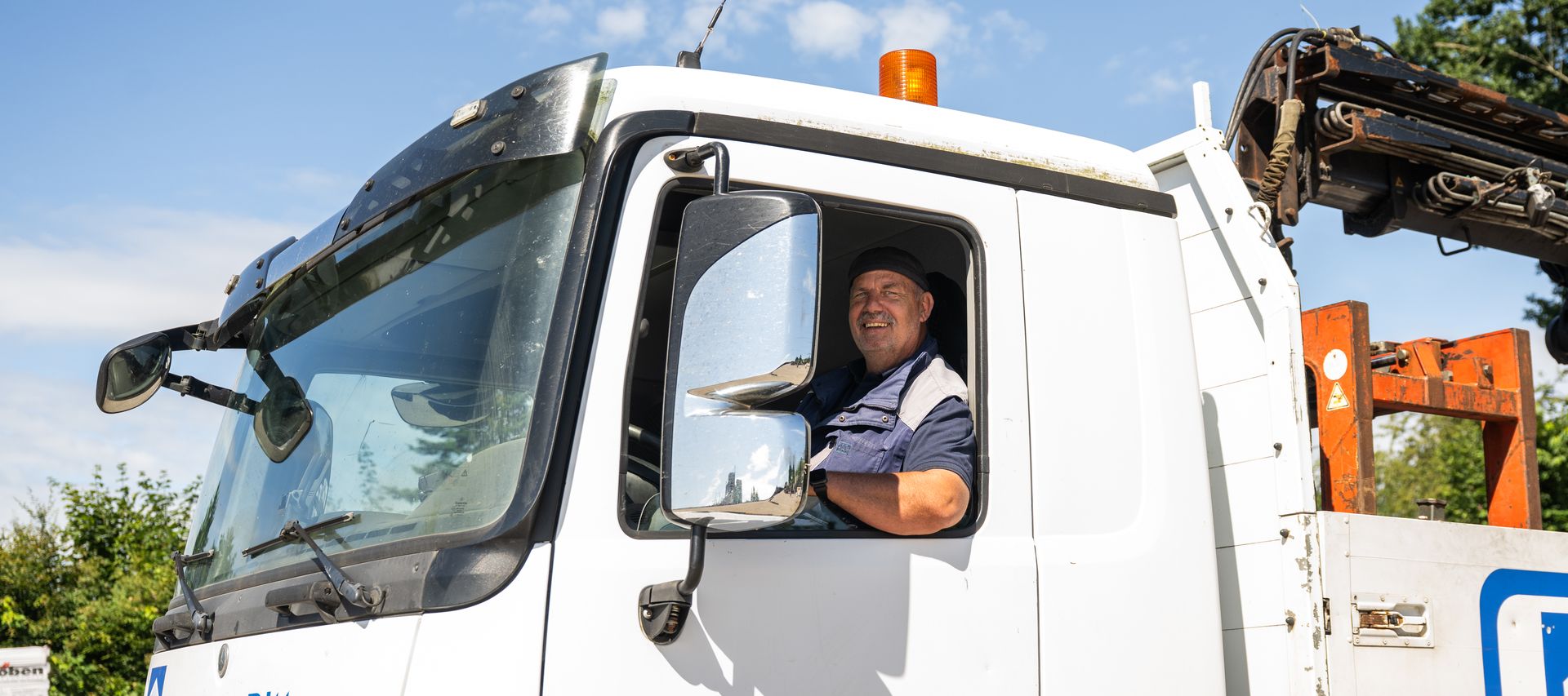 Ein Lkw-Fahrer von bauXpert Dittmer sitzt lächelnd in seinem Führerhaus und blickt aus dem geöffneten Fenster.