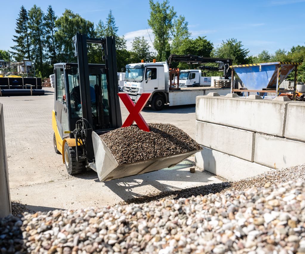 Ein Gabelstapler mit Schaufel lädt Kies auf dem Lagerplatz von bauXpert Dittmer, im Hintergrund sind Lkw, Lagerflächen und Baustoffe zu sehen.