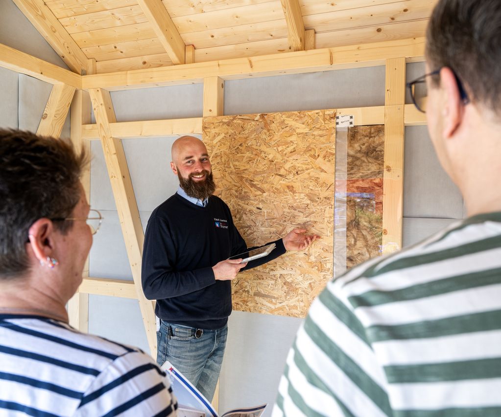 Fachberater erklärt Kunden den Wandaufbau im Holzrahmenbau: OSB-Platte, Dämmung und Dampfbremse am Musterexponat