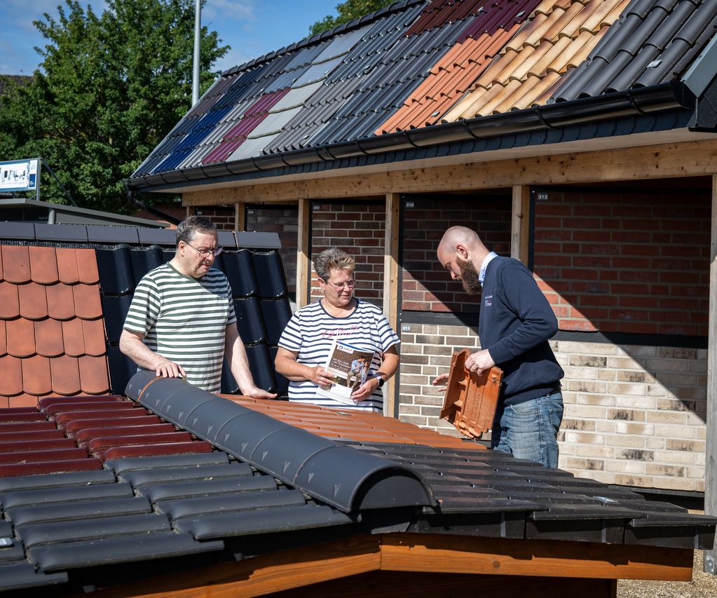 Fachberater zeigt Tonziegel am Musterdach – zwei Kund:innen vergleichen Farben und Profile vor der Ziegel- und Klinkerausstellung