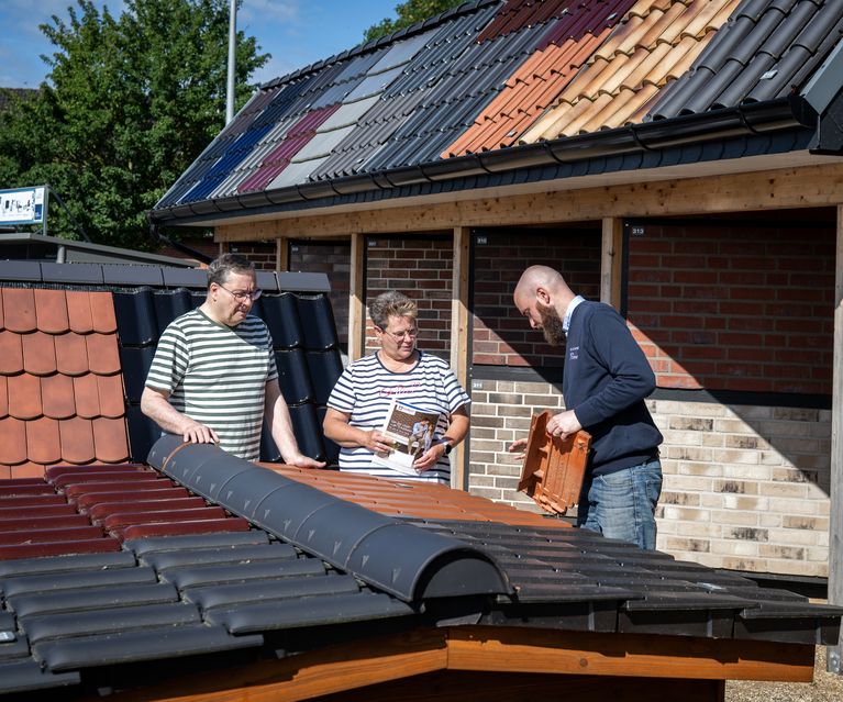 Fachberater zeigt Tonziegel am Musterdach – zwei Kund:innen vergleichen Farben und Profile vor der Ziegel- und Klinkerausstellung