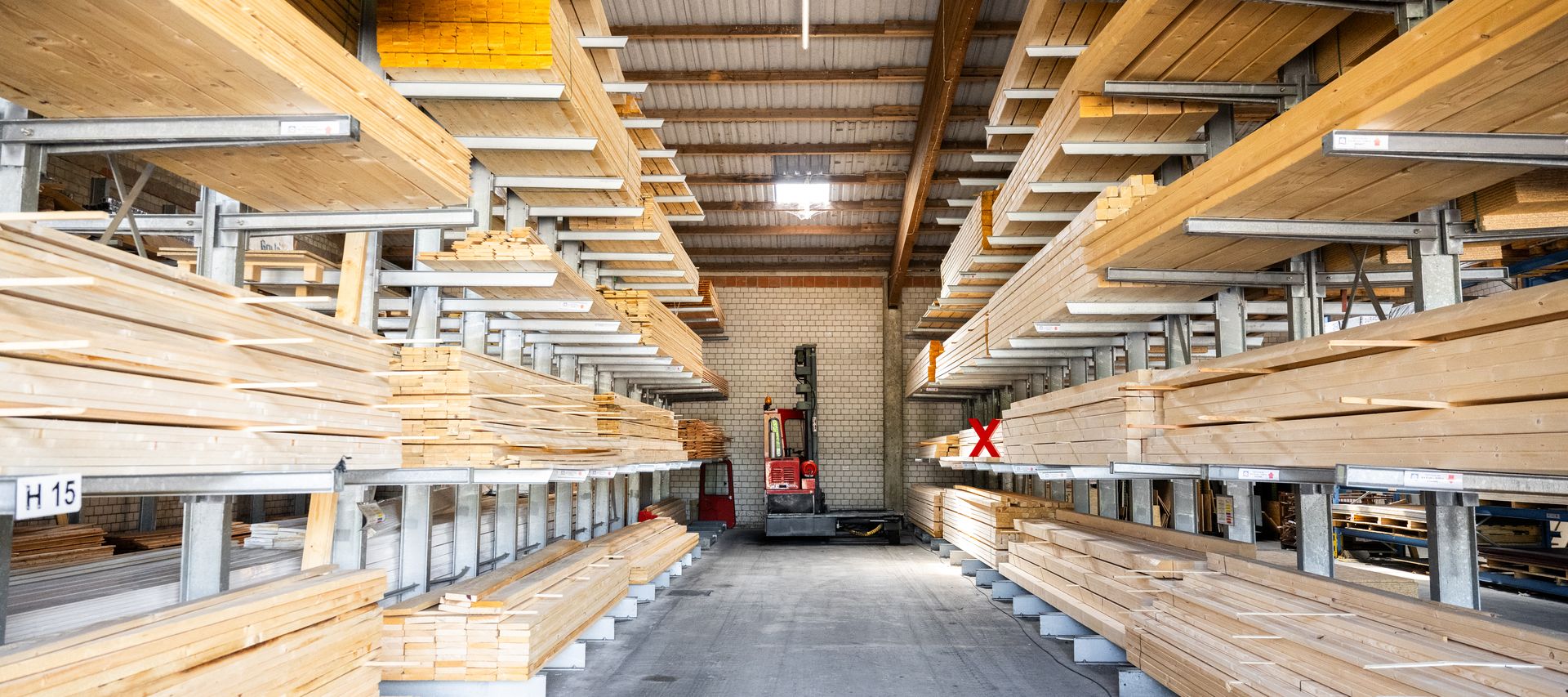 Holzlagerhalle mit Kragarmregalen voller Konstruktionsholz; Stapler am Gangende