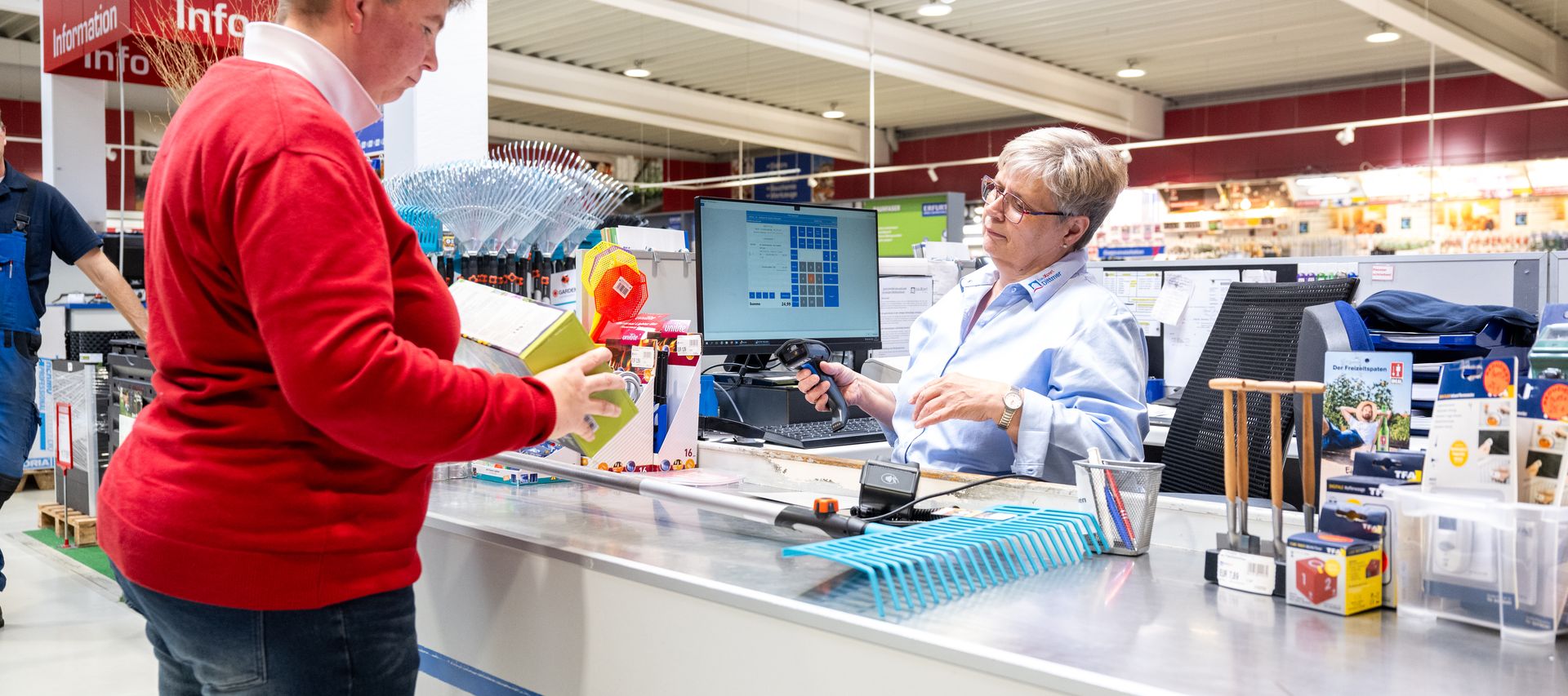Mitarbeiterin von bauXpert Dittmer in Lütjenburg berät eine Kundin an der Kasse und scannt Produkte im Fachmarkt.