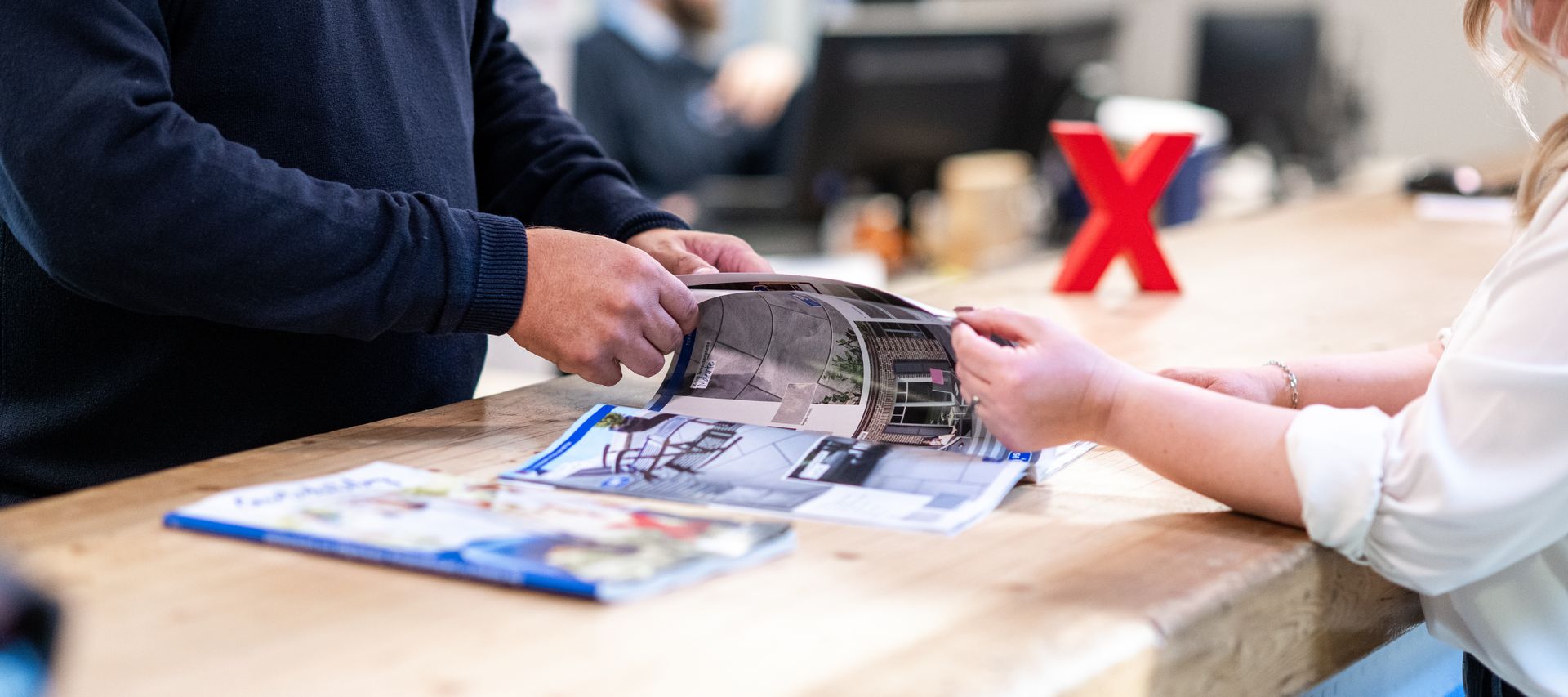 Beratungssituation am Tresen bei bauXpert Dittmer: Zwei Personen blättern gemeinsam in einem Musterkatalog für Pflastersteine