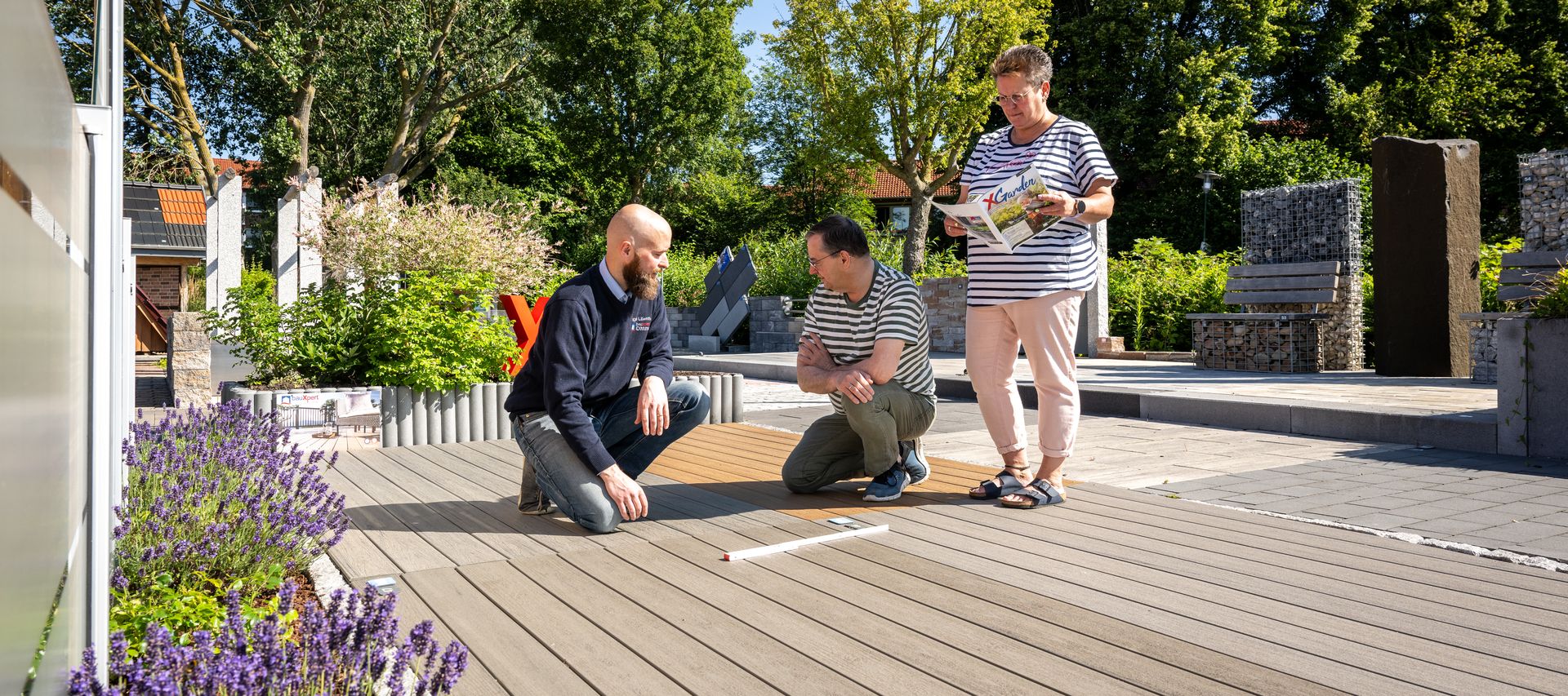 Mitarbeiter berät zwei Kunden zu Terrassendielen in der Gartenausstellung von bauXpert Dittmer in Lütjenburg
