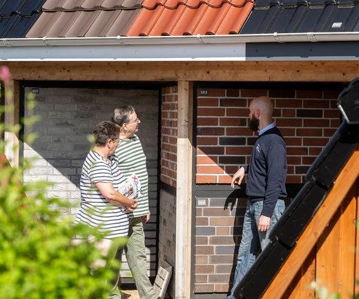Fachberater erklärt einem Paar unterschiedliche Klinkerverblender an der Musterwand im Außenbereich von bauXpert Dittmer