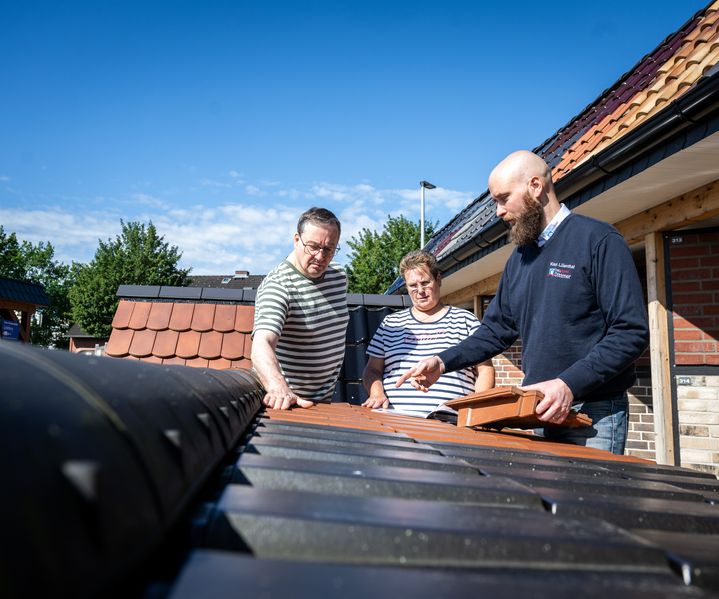 Fachberater von bauXpert Dittmer zeigt einem Kundenpaar verschiedene Dachziegel in der Außenausstellung