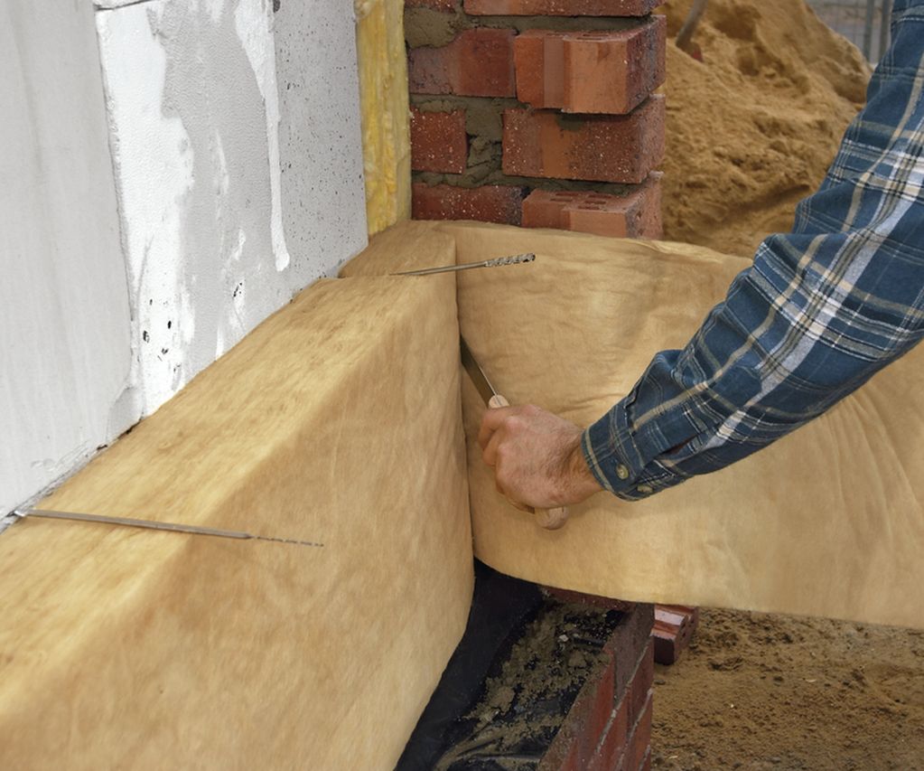 Arbeiter bringt Kerndämmmaterial an Hausfassade an