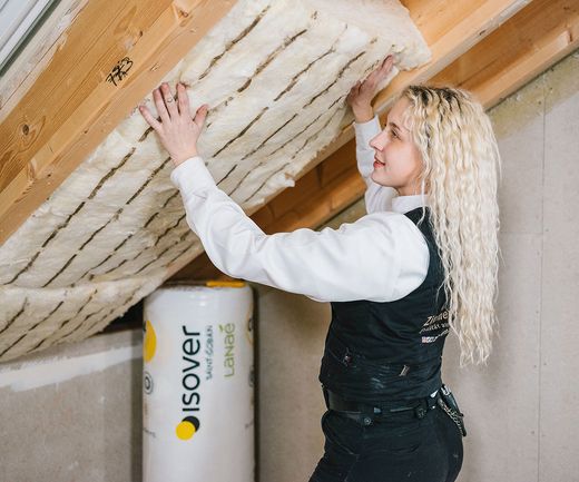 Dachdämmstoffe werden von einer Handwerkerin in die Sparren vom Dachstuhl gedrückt