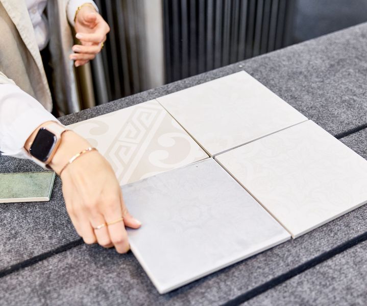 Fliesenberaterin, die weiße Fliesen mit dezenten Mustern auf einer grauen Fläche anordnet.