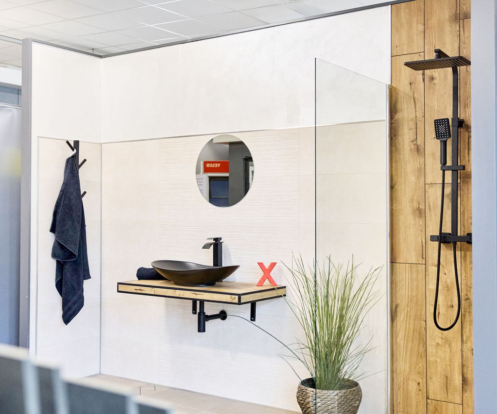 Fliesenausstellung: Modernes Badezimmer mit rundem Spiegel, Aufsatzwaschbecken, schwarzen Armaturen, Holzfliesen, Handtuch und Topfpflanze auf dem Boden