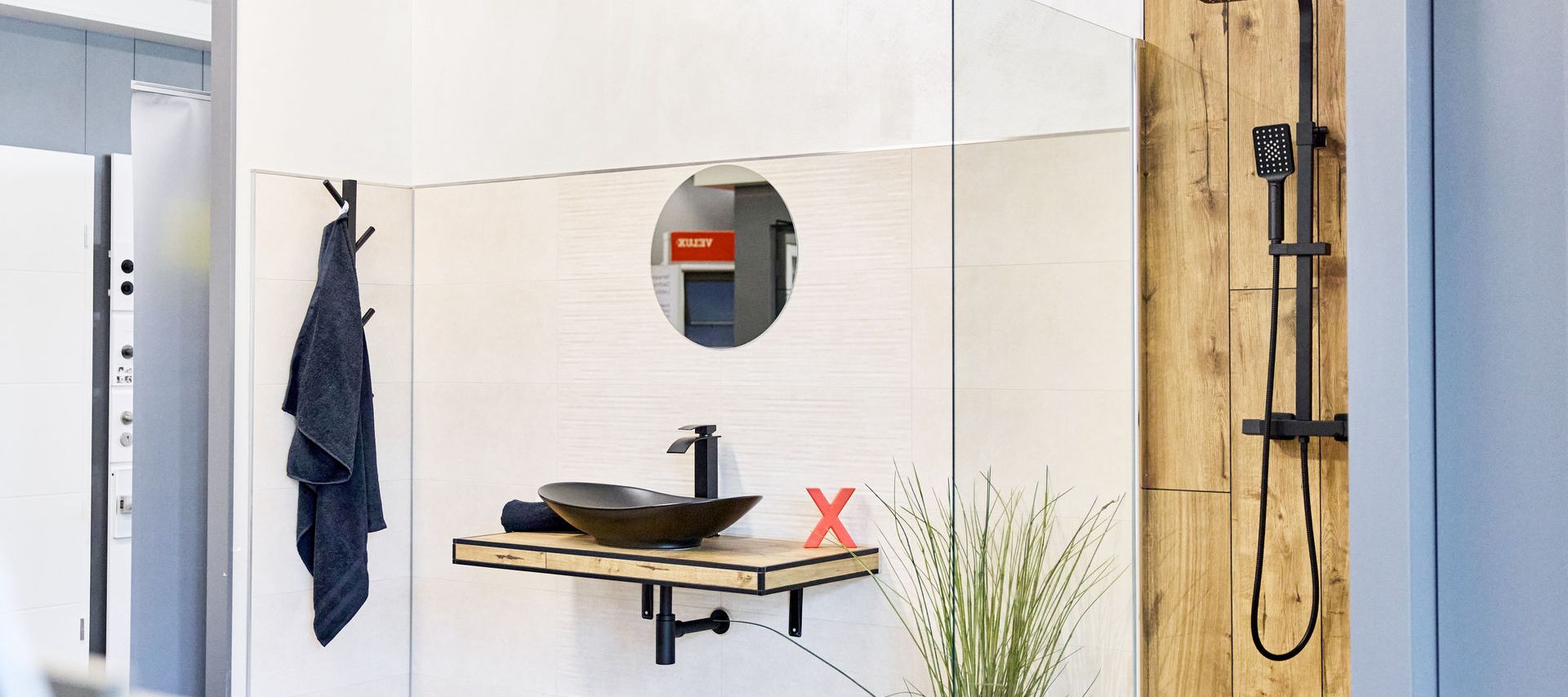 Fliesenausstellung: Modernes Badezimmer mit rundem Spiegel, Aufsatzwaschbecken, schwarzen Armaturen, Holzfliesen, Handtuch und Topfpflanze auf dem Boden