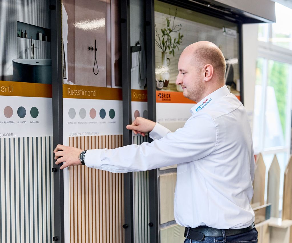 Ein Fliesenberater mit weißem Hemd betrachtet Fliesenmuster, die auf Tafeln in einer Fliesenausstellung bei Bremen präsentiert werden