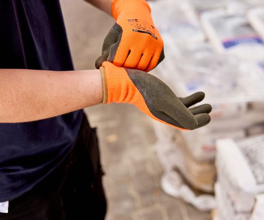 orangene Arbeitshandschuhe werden von Lagermitarbeiter angezogen
