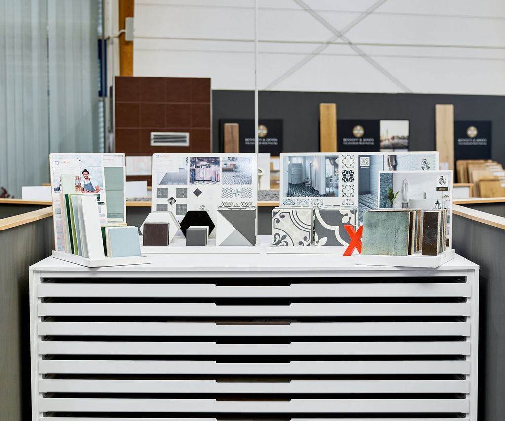 Fliesenausstellung mit architektonischen Designmustern auf weißem Präsentationsstand, inklusive Fliesen, Muster und Materialproben in einem Showroom.