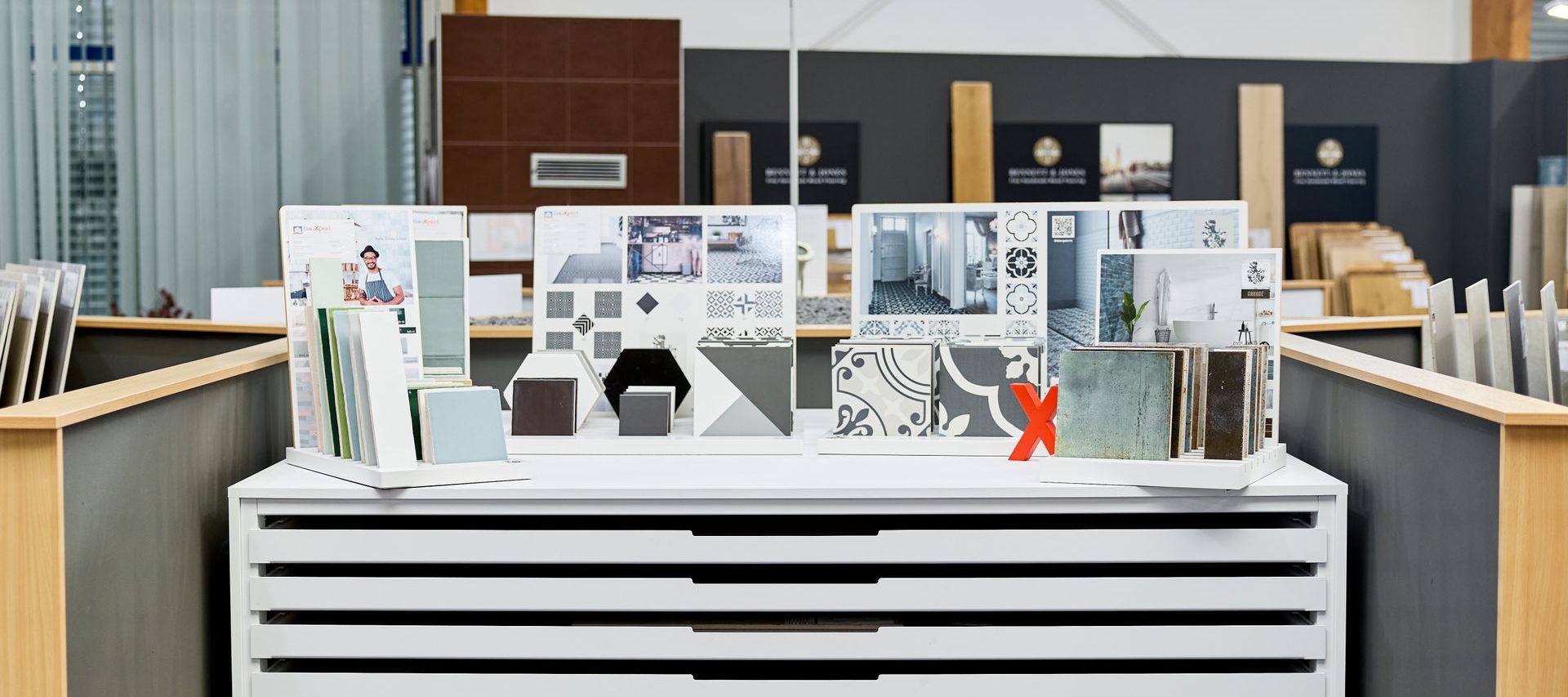 Fliesenausstellung mit architektonischen Designmustern auf weißem Präsentationsstand, inklusive Fliesen, Muster und Materialproben in einem Showroom.