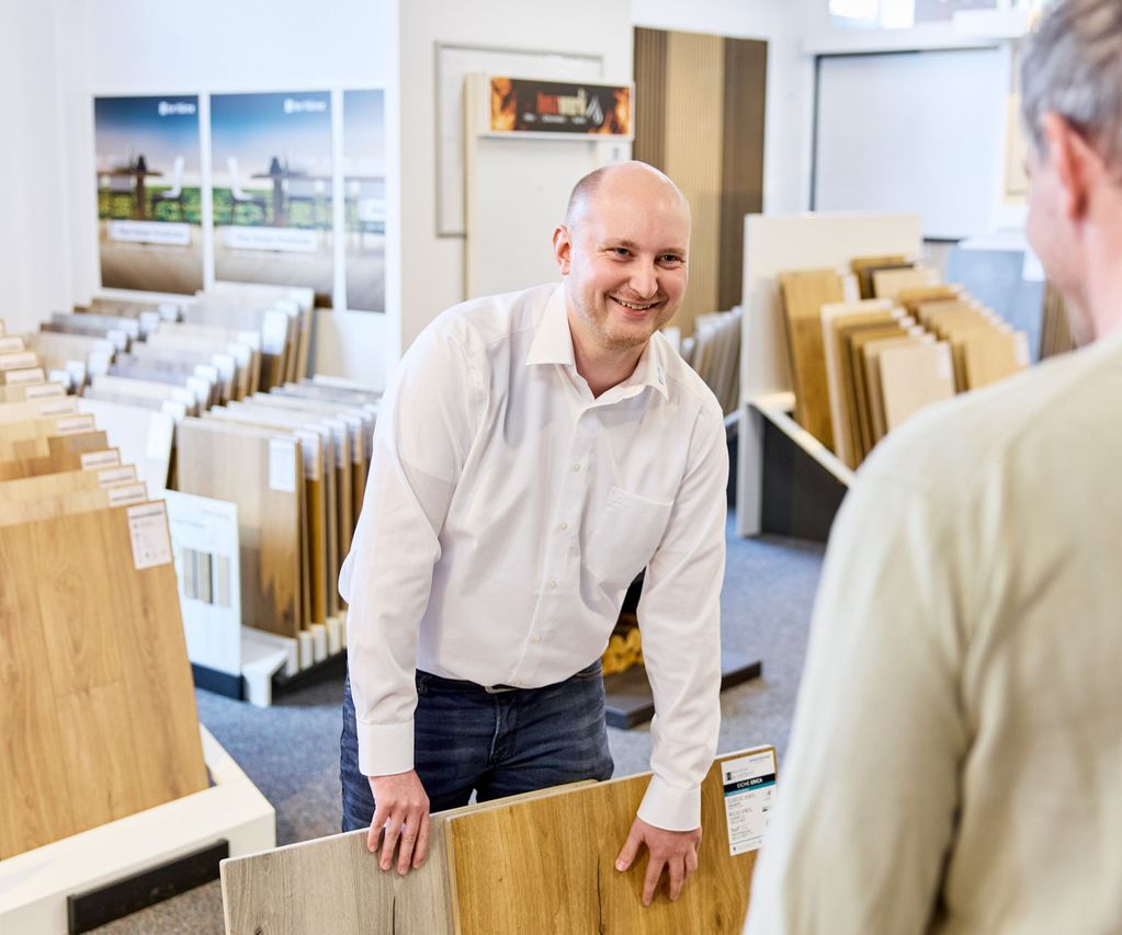 Fachberater für Bodenbeläge zeigt Kunden Musterbeispiele verschiedener Dekore
