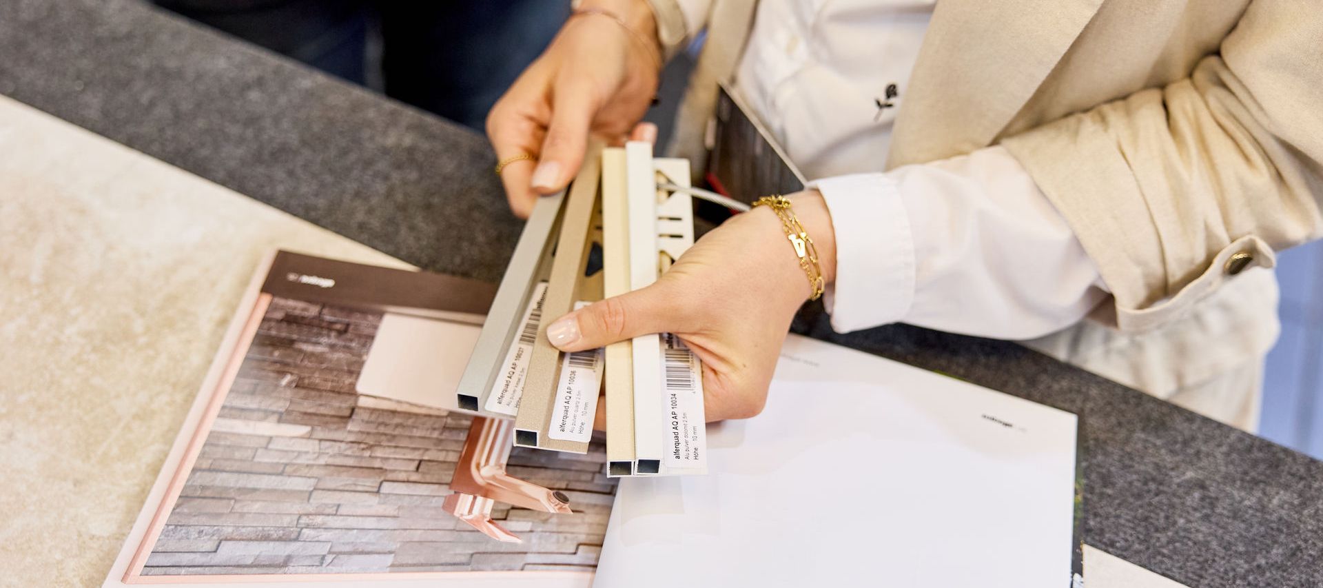 Fliesenberaterin hält Fliesenschienen über ein geöffnetes Fliesenmagazin,  zur Auswahl von Farbe und Materialien
