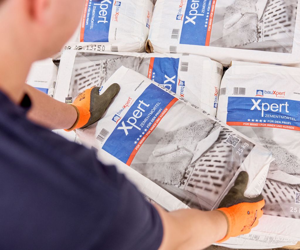 orangene Arbeitshandschuhe werden von Lagermitarbeiter am Zementmörtelsack benutzt