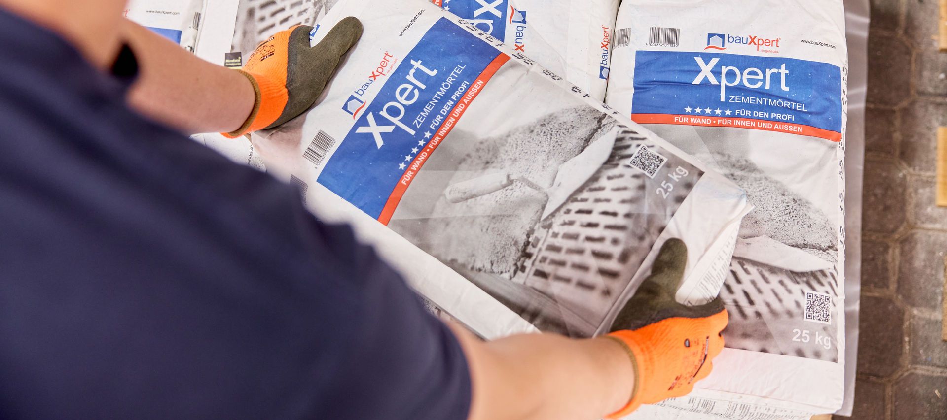 orangene Arbeitshandschuhe werden von Lagermitarbeiter am Zementmörtelsack benutzt