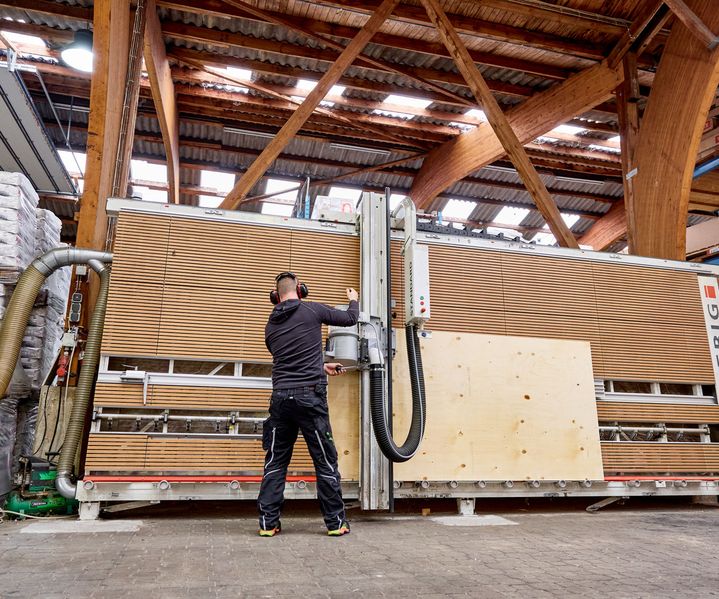 Mitarbeiter schneidet Sperrholzplatten mit großer Plattensäge im Baustoffhandel