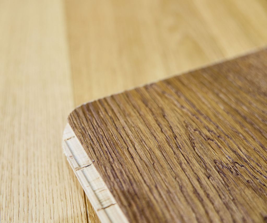 Close-up of a wooden table corner with a visible layered edge, showcasing two different wood grain textures and colors.