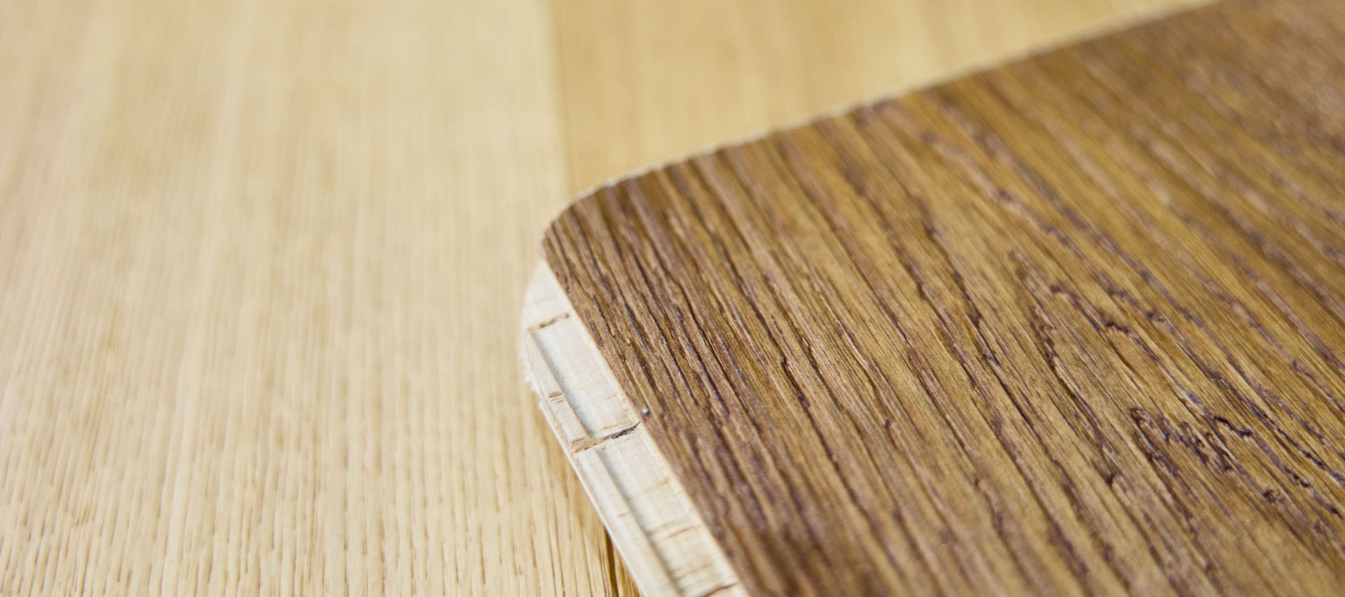 Close-up of a wooden table corner with a visible layered edge, showcasing two different wood grain textures and colors.