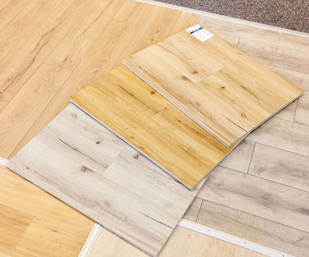 Three samples of wood vinyl flooring in light, medium, and dark shades are displayed on a showroom floor.