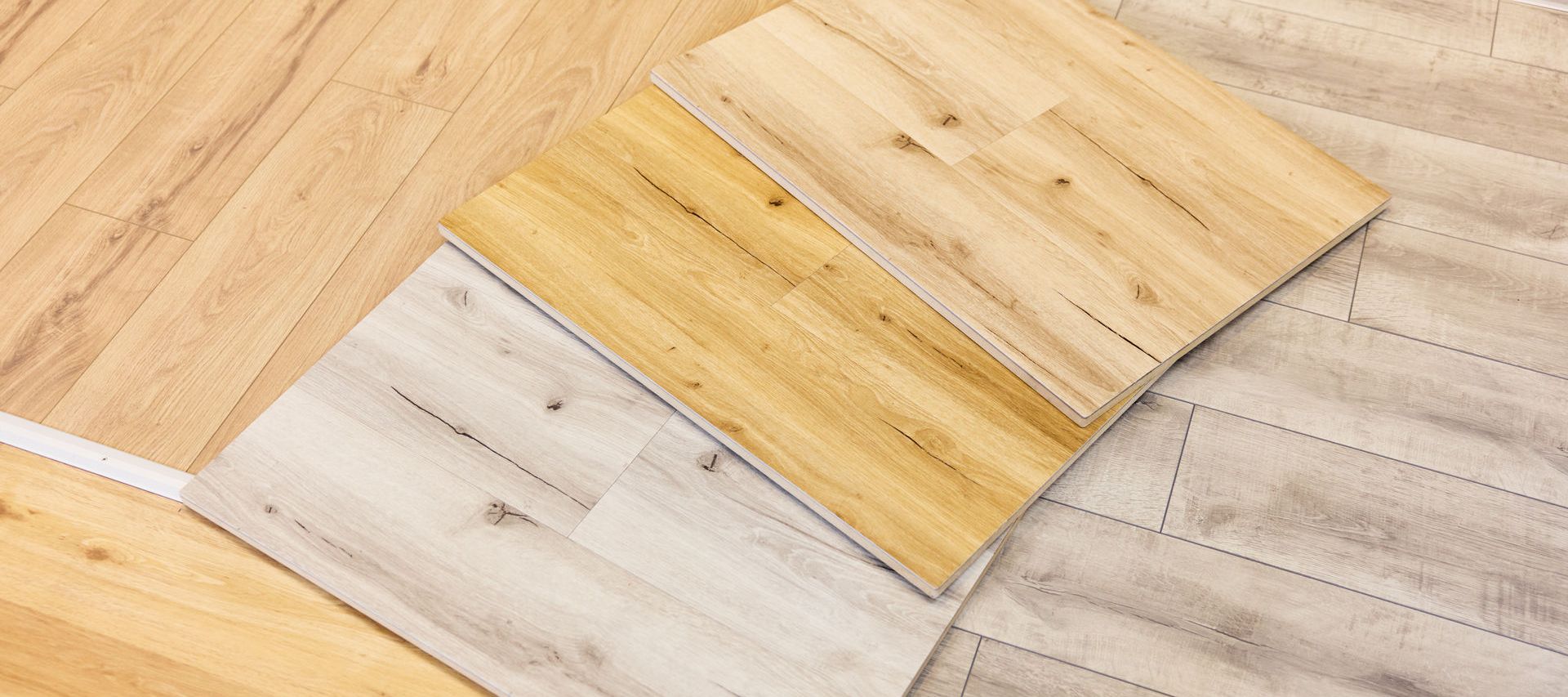 Three samples of wood vinyl flooring in light, medium, and dark shades are displayed on a showroom floor.