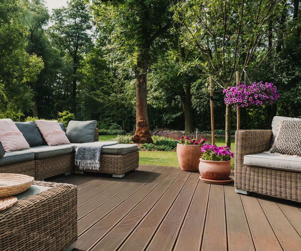 Terrasse mit Rattan-Sitzgruppe, Hängesessel und Gartenmöbeln vor dicht bepflanztem Garten