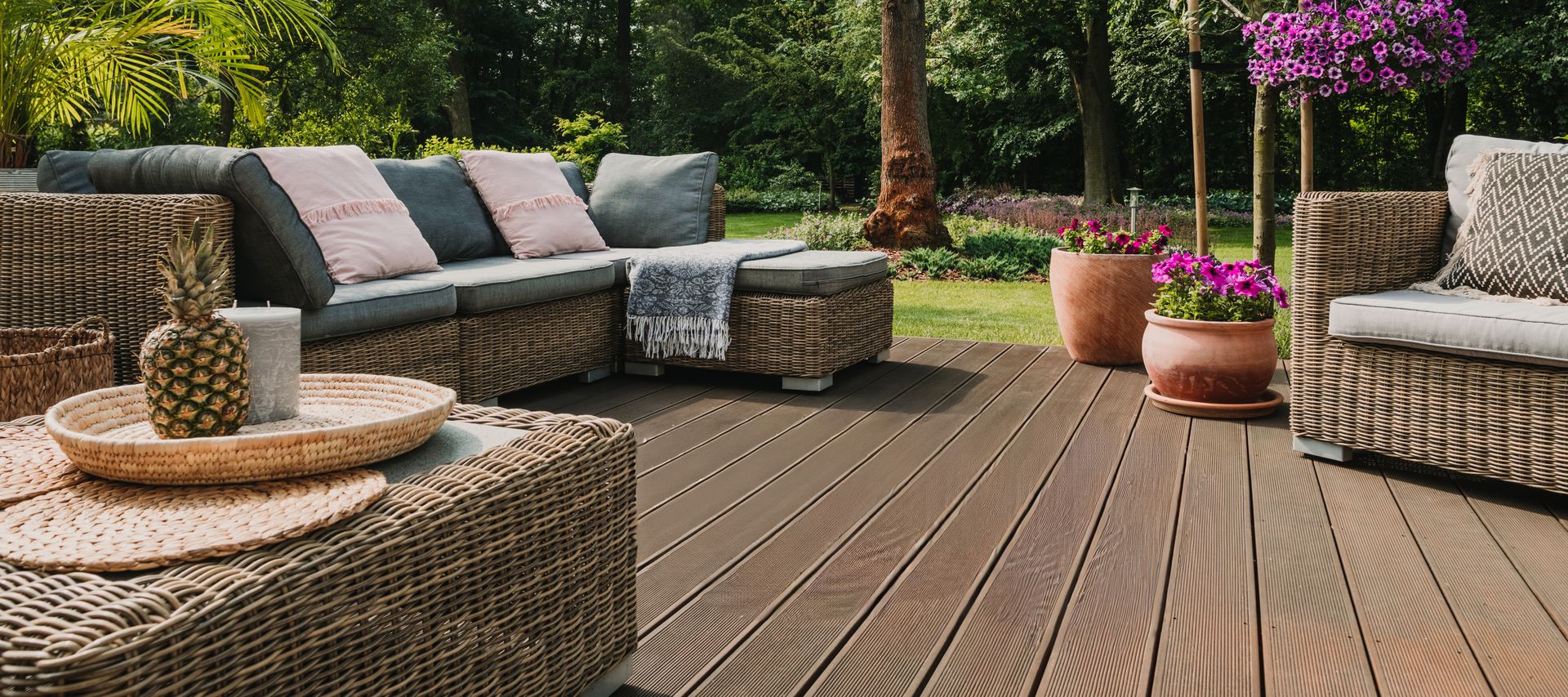 Terrasse mit Rattan-Sitzgruppe, Hängesessel und Gartenmöbeln vor dicht bepflanztem Garten