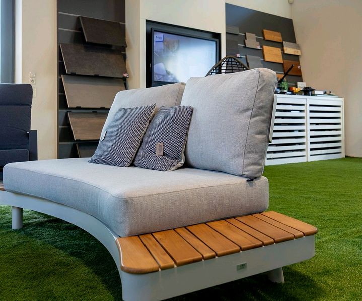 Gepolstertes Outdoor-Sofa mit Holzablage in einer Gartenmöbel-Ausstellung.