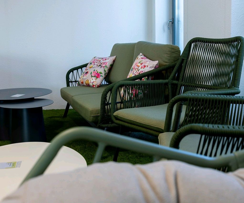 Outdoor-Sitzgruppe mit grünem Sofa, Sesseln und Beistelltischen in einer Gartenmöbel-Ausstellung.