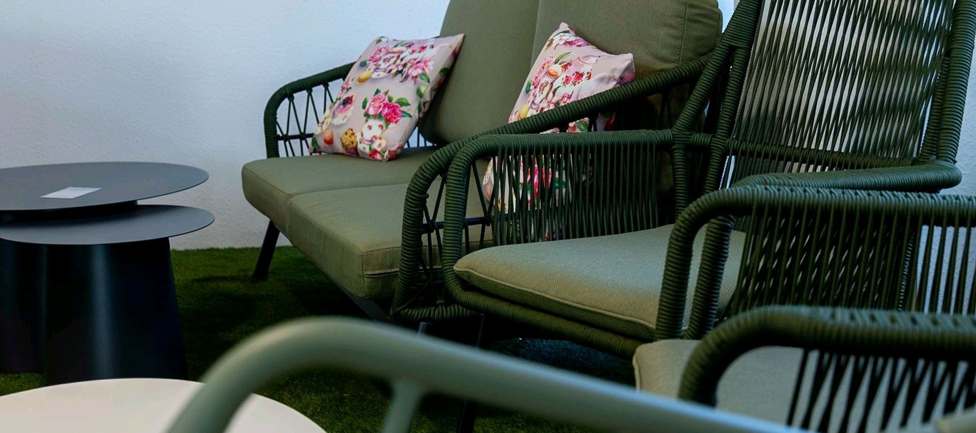 Outdoor-Sitzgruppe mit grünem Sofa, Sesseln und Beistelltischen in einer Gartenmöbel-Ausstellung.