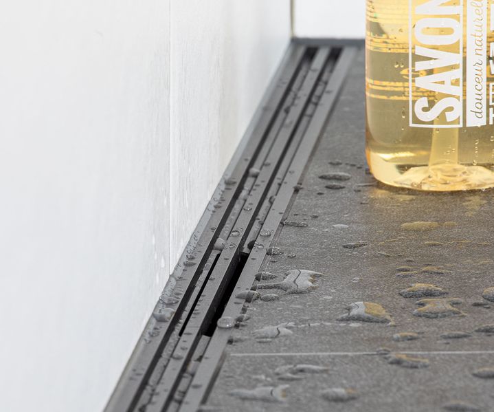 Schwarze Duschrinne entlang einer gefliesten Wand mit Wassertropfen auf dunklen Bodenfliesen