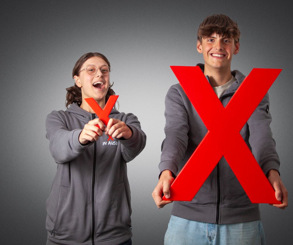 zwei Azubis halten das kleine und das große rote X in die Kamera und lächeln