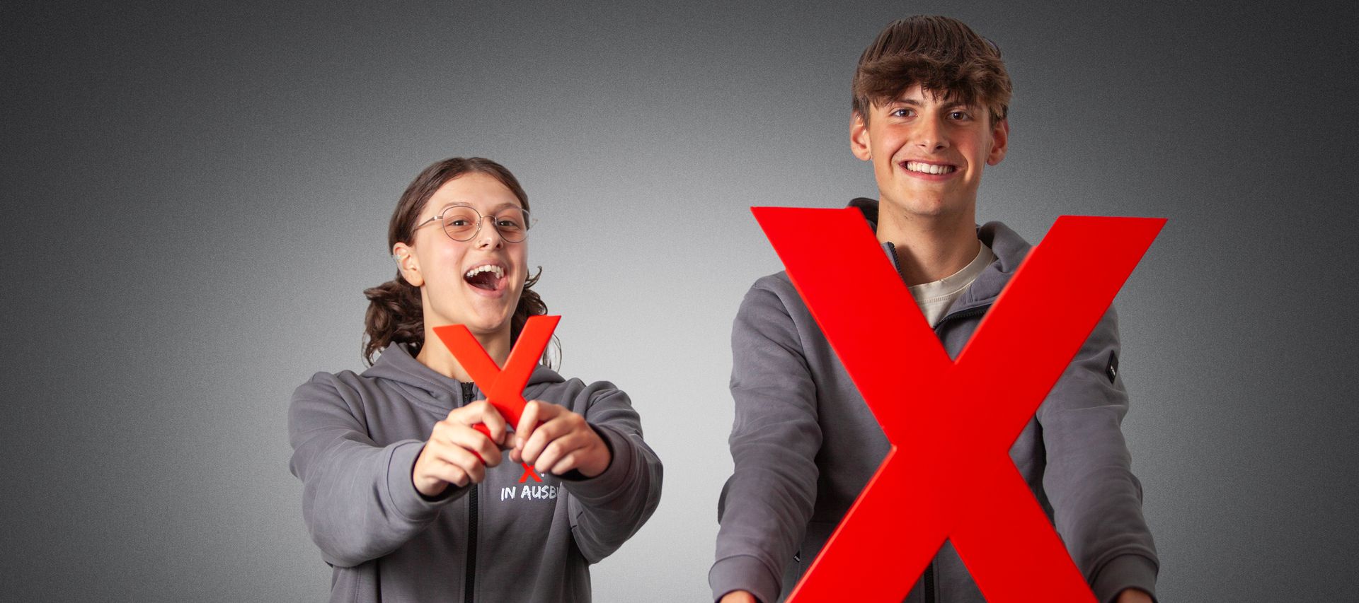 zwei Azubis halten das kleine und das große rote X in die Kamera und lächeln