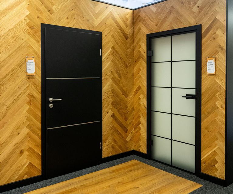 Links eine schwarze Tür mit silberenen Elemente, rechts eine Glastür mit schwarzen Elemtnen sowie einer schwarzen Zarge. Ausstellung von bauXpert Gr Beilage Vechta