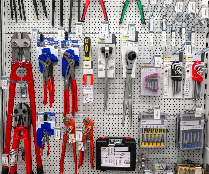 Werkzeugwand mit Zangen, Schraubenschlüsseln, Ratschen und Bits übersichtlich an einer Lochwand im Fachmarkt präsentiert.