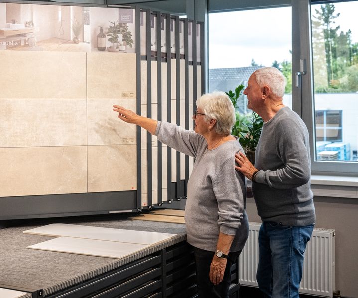 Zwei Perosnen schauen sich in der Fliesen-Ausstellung von bauXpert Gr. Beilage in Vechta die Fliesen an. 20250905_bauXpert_GrBeilage_Beratung_Fliese_Kunden