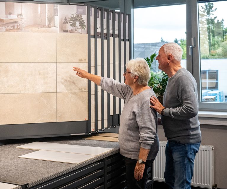Zwei Perosnen schauen sich in der Fliesen-Ausstellung von bauXpert Gr. Beilage in Vechta die Fliesen an. 20250905_bauXpert_GrBeilage_Beratung_Fliese_Kunden