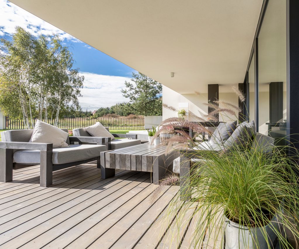 Terrasse mit grauen Terrassendielen, Sitzgruppe und Pflanzgefäßen entlang einer modernen Glasfassade