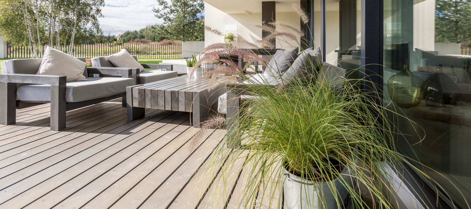 Terrasse mit grauen Terrassendielen, Sitzgruppe und Pflanzgefäßen entlang einer modernen Glasfassade