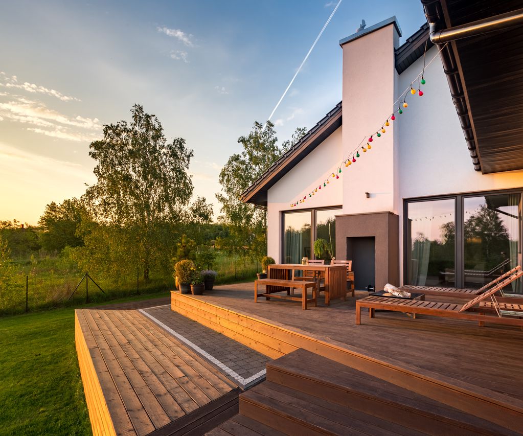 Mehrstufige Holzterrasse mit Sitzgruppe und Liegen an einem Wohnhaus mit Blick in den Garten bei Abendlicht