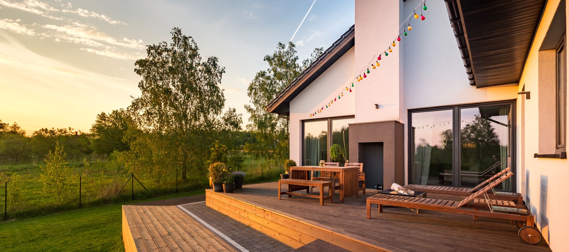 Mehrstufige Holzterrasse mit Sitzgruppe und Liegen an einem Wohnhaus mit Blick in den Garten bei Abendlicht