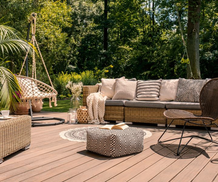Holzterrasse mit Rattan-Sitzgruppe, Hängesessel und Gartenmöbeln vor dicht bepflanztem Garten