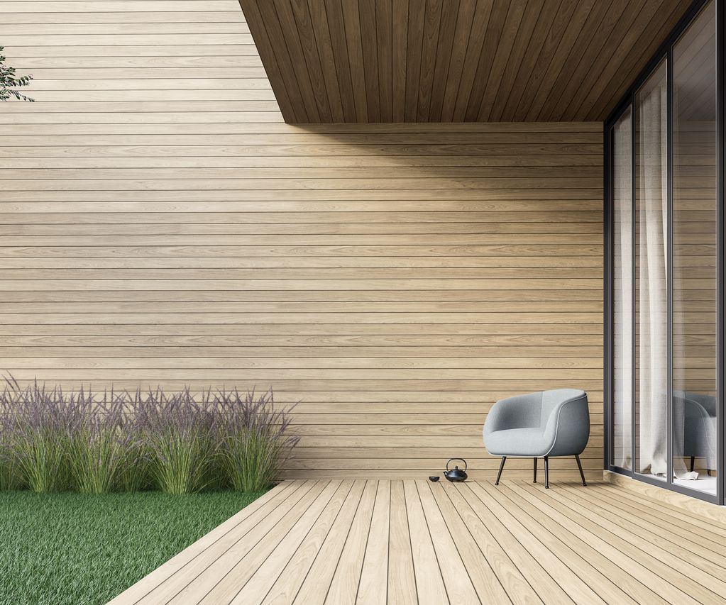 Helle Terrassendielen vor einer Holzfassade mit Glasfront, Rasenfläche und Ziergräsern